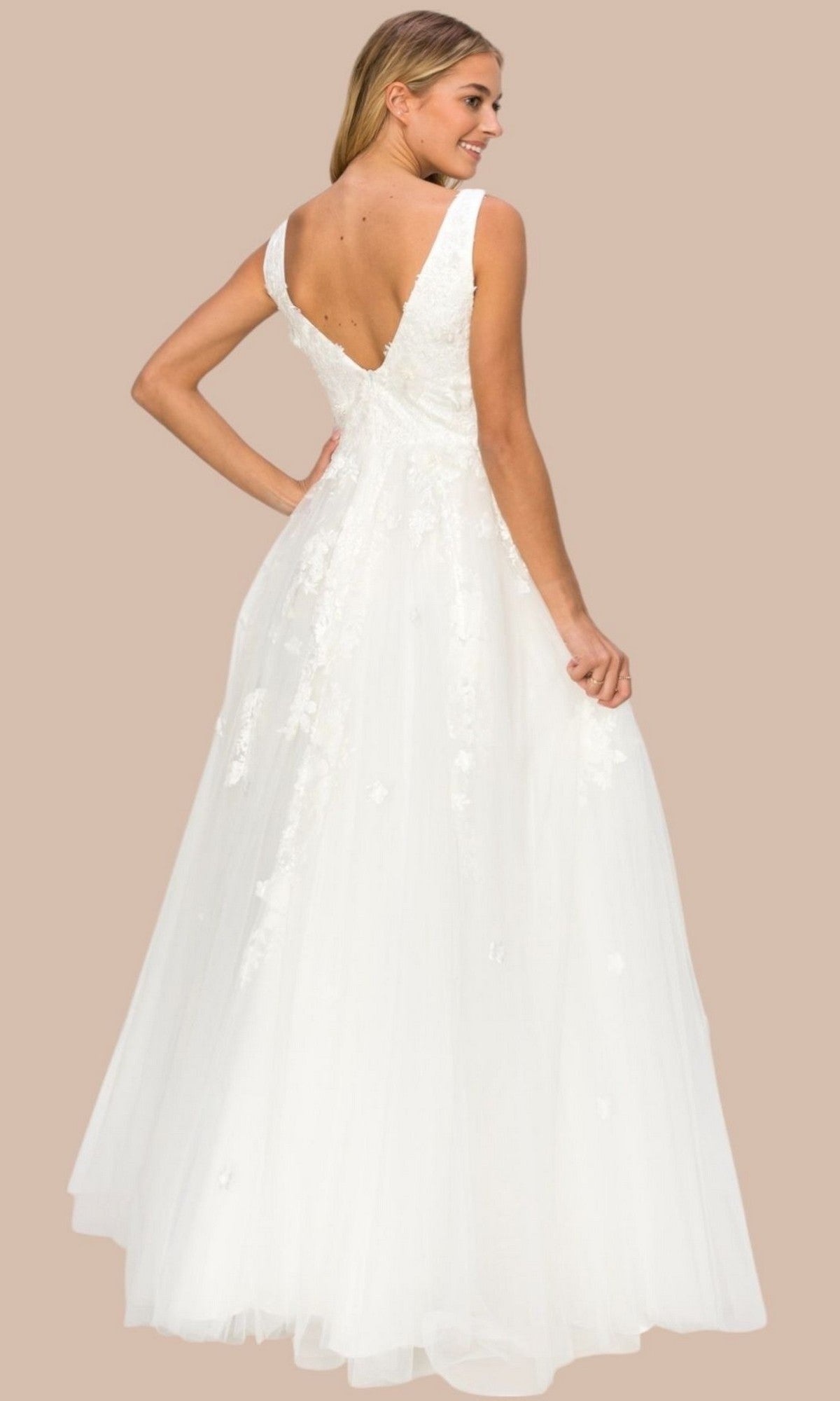 A woman in a sleeveless white bridal gown featuring delicate 3D floral lace appliques and a deep V-back stands against a beige background, looking over her shoulder—the Long Formal Dress: Cinderella Couture 8040J.